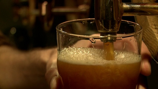 一个男人在酒吧里拖着一品脱啤酒的特写。视频素材