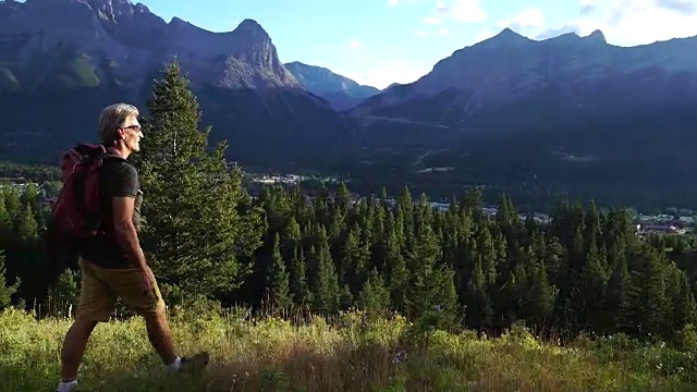 男性徒步旅行者穿过村庄和山谷上方的高山草甸视频素材