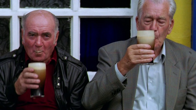 肖像:爱尔兰艾沃萨酒吧前，两名年长男子坐在长凳上喝黑啤酒视频素材