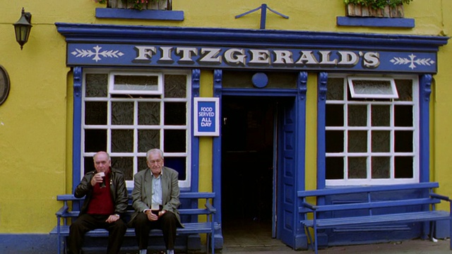 爱尔兰Avoca“Fitzgerald’s”酒吧前，两名年长男子一边喝着啤酒，一边坐在长凳上视频下载