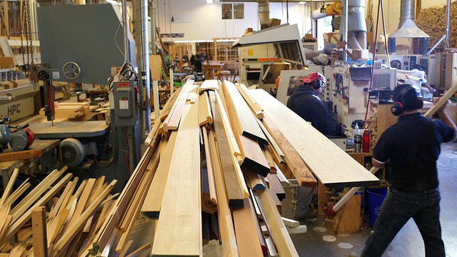 运动控制，在定制的木工车间，垂直起重机在堆放的原木片的两端移动，工人扛着木板通过框架视频素材