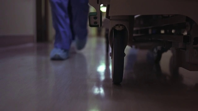 医院病床通过走廊时车轮的近角度。在床边快速行走的护士或医生的脚和腿。那个人穿着手术服。可能是紧急情况视频下载