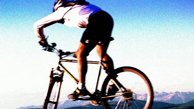颗粒状的慢动作男性山地自行车在镜头前跳跃，以山脉为背景/科罗拉多视频下载