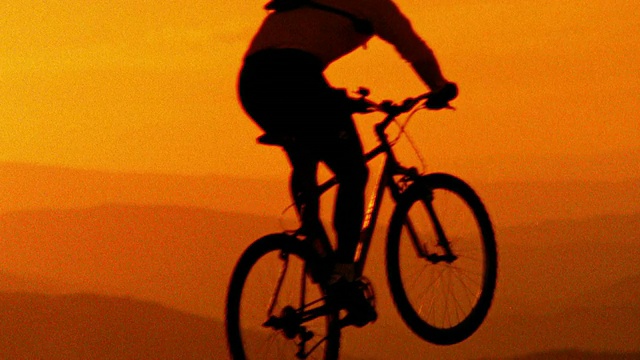 橙色慢镜头男性山地自行车跳跃在镜头前，山的背景/ CO视频素材