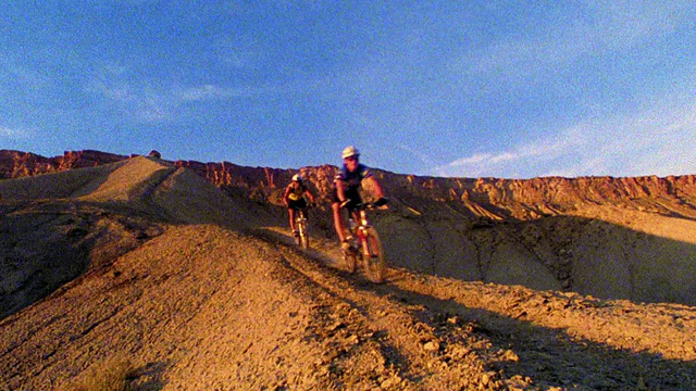 在科罗拉多西部沙漠的土坡上，两名山地自行车男骑着自行车经过相机视频素材