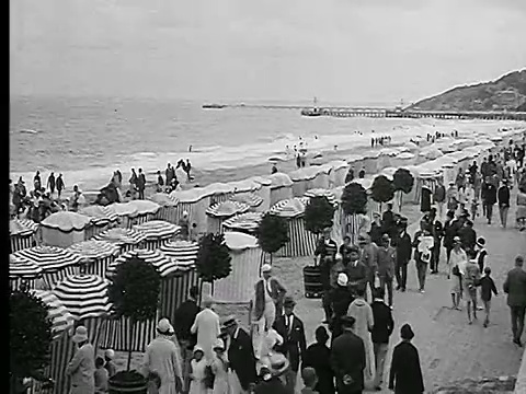 20世纪20年代的高角度雨伞+人群散步+游泳在法国多维尔海滩视频下载