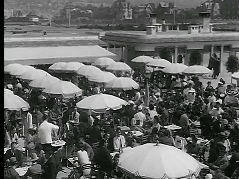 20世纪30年代的高角度PAN拥挤的木板路+户外咖啡馆旁边的海滩/多维尔，法国诺曼底视频下载