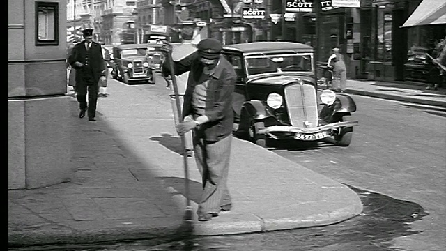 1936年，男子在街角扫水/交通+人行道上的行人/巴黎视频素材