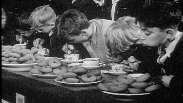 20世纪40年代/50年代在比赛/新闻短片中，一排男孩在餐桌上吃甜甜圈视频下载