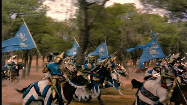重现一群6世纪的骑士拿着剑和旗帜在马背上跑过树林的场景视频素材