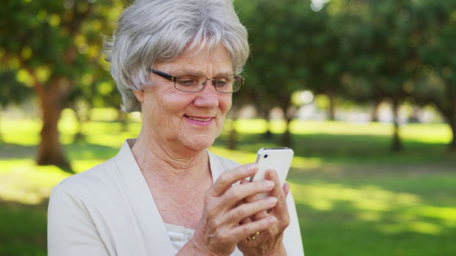 老女人在公园用智能手机发短信视频素材