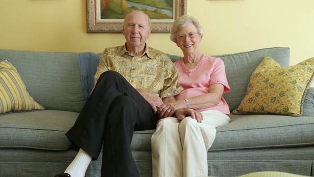 一对老夫妇紧挨着坐在灰色沙发上的静态照片。视频下载