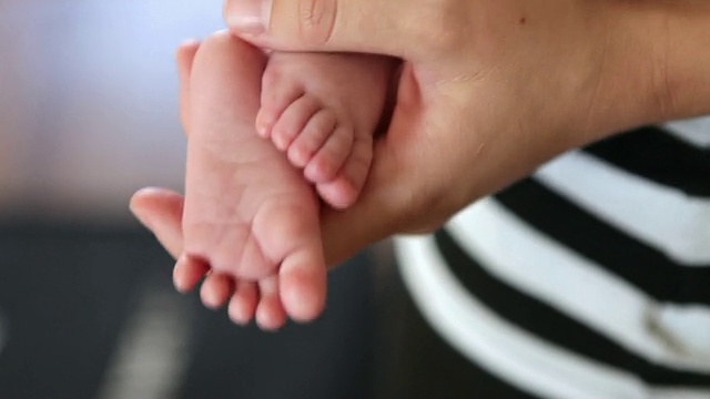 一个年轻人的手牵着一个婴儿的两只脚的特写。视频素材