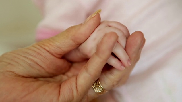 一位老妇人牵着婴儿的手的特写镜头。视频素材