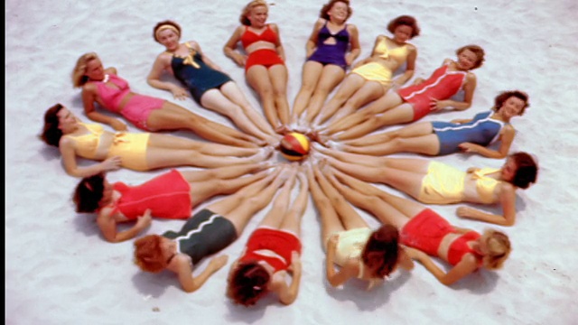 20世纪40年代/50年代的高角度妇女穿着泳衣躺在沙滩上，中间是沙滩球/开始扔球视频下载