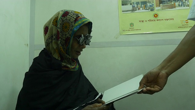 孟加拉国农村的一个医疗保健非政府组织在一艘医疗船上为一名老年妇女提供新眼镜之前，该妇女接受了眼科检查和验光师的检查视频下载