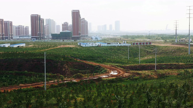 慢速镜头从左到右穿过中国的一片绿色景观，在一些距离之外，有一座新开发的高楼大厦视频下载