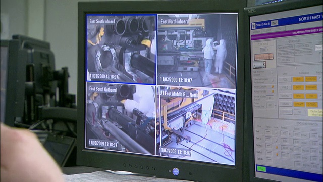 一个技术员在工作台上看两个电脑屏幕和一个安全监视器。视频下载