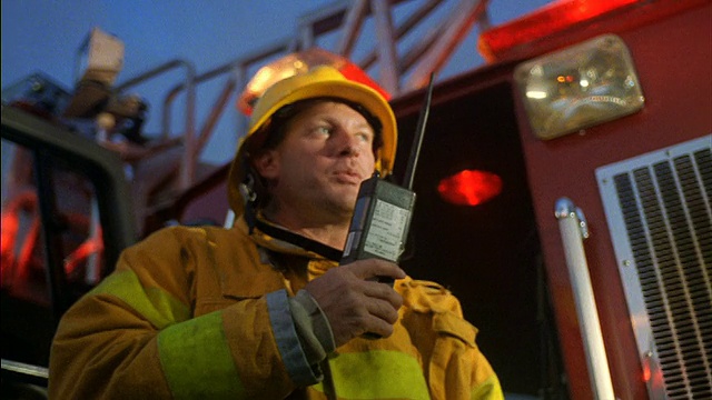 低角度的消防队员对着对讲机说话，周围环顾，背景是消防车视频素材