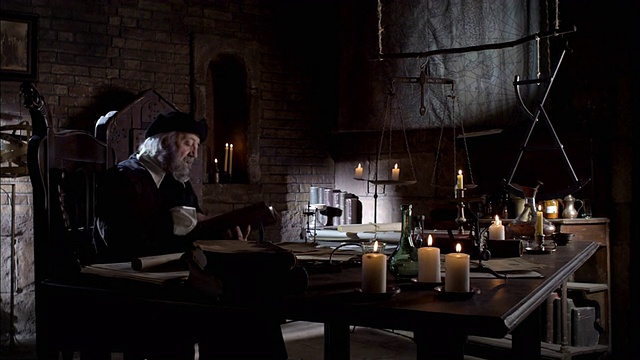 诺查丹玛斯坐在点着蜡烛的桌子前，开始读一本书。视频下载