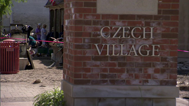 砖标上的青铜字母表明是捷克村庄，背景是店主在清理洪水留下的废墟。视频下载