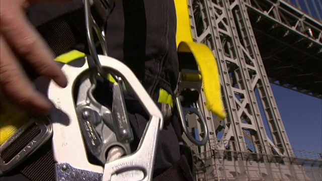 一名维修工站在纽约市一座悬索桥的基座上，正在固定他的装备。视频素材