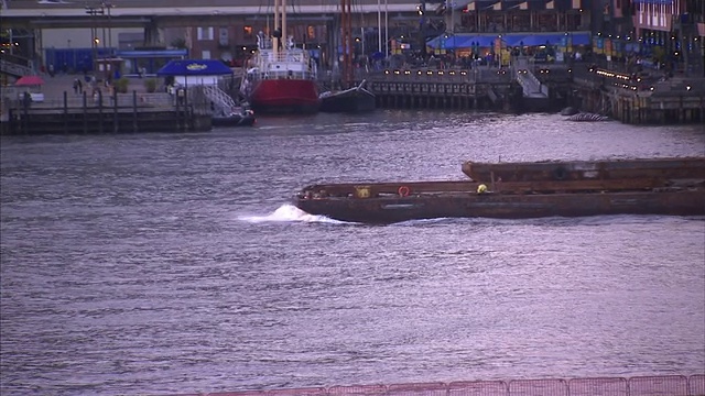 一艘拖船推着一艘驳船穿过纽约市的一个港口。视频素材