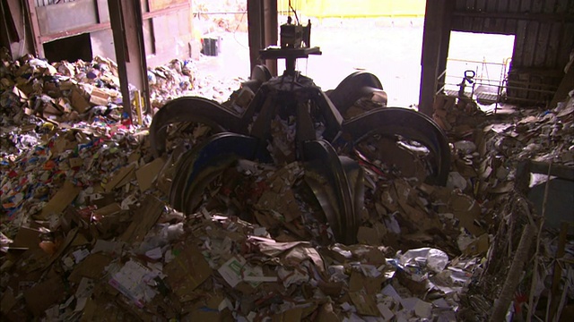 在回收设施里，一个爪子抓钩摊开在一大堆纸上。视频下载