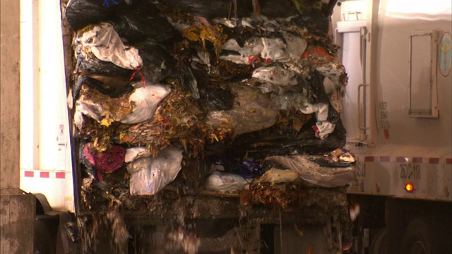 一辆垃圾车将垃圾倾倒到收集设施的一个坑里。视频下载