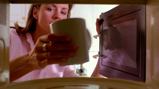 近微波炉看女人把咖啡杯放在微波炉里，加热+取出视频素材