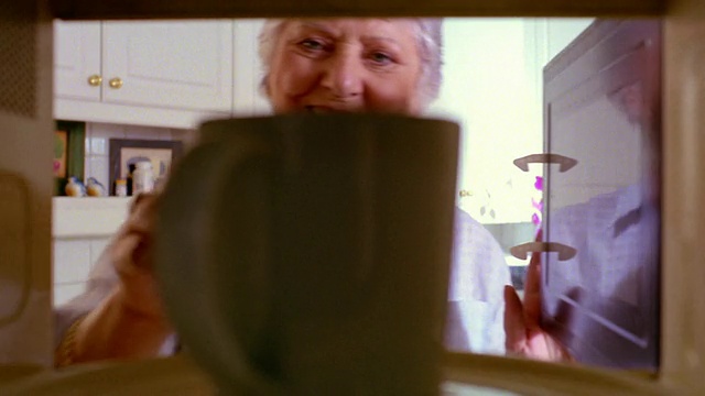 近微波炉视点资深女士将咖啡杯放入微波炉，加热+取出视频素材