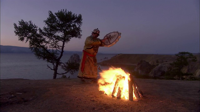 一位穿着传统服装的俄罗斯人围着火堆打鼓跳舞。视频下载
