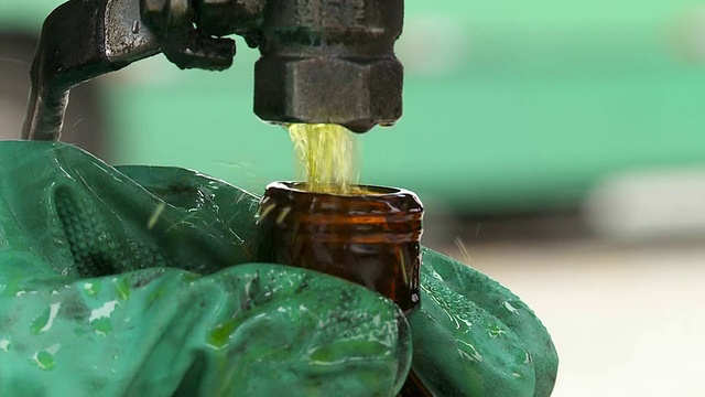 一只戴着手套的手拿着一个瓶子，生物燃料正往瓶子里倒。视频下载