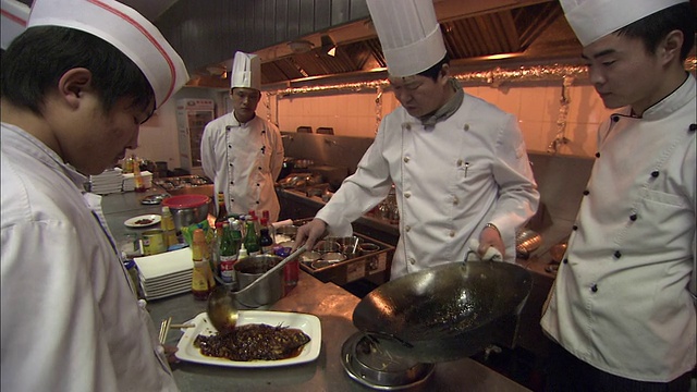 一个厨师在另一个厨师把配菜舀到盘子里的鱼上后擦拭盘子。视频素材