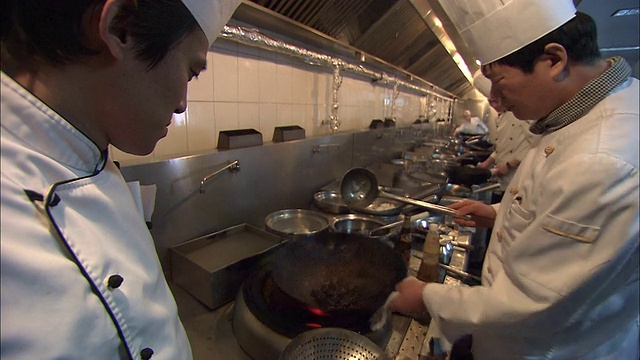 一名受训厨师看着主厨在锅里煮蘑菇，然后把它们倒进一个待用的盘子里。视频素材
