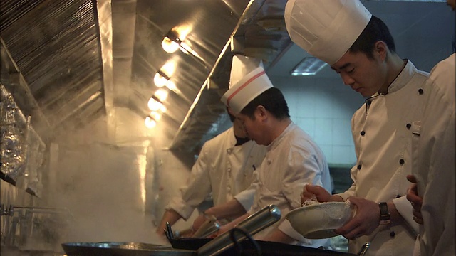 在一间厨房里，三个厨师在热气腾腾的锅上做饭。视频素材
