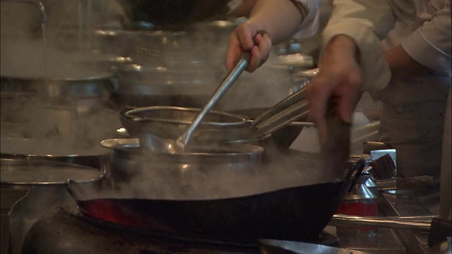 当餐厅厨师把热水舀进锅里，在明火上擦洗平底锅时，蒸汽上升。视频素材