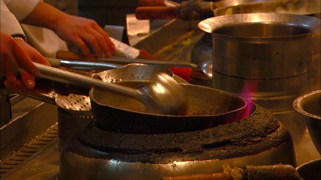餐馆的厨师在明火上用平底锅烹饪食物。视频素材