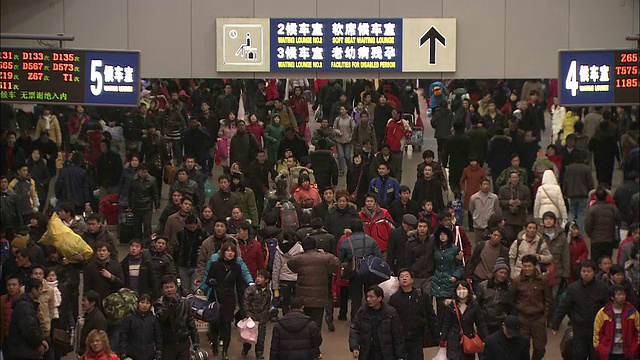 在北京西站，一个电子指示牌在人群上方显示着列车时刻表。视频下载