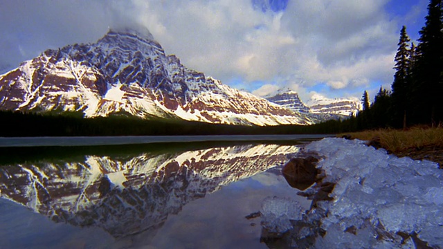 湖面上的冰/雪山+背景中的时间流逝云+在湖/加拿大反射的观点视频素材