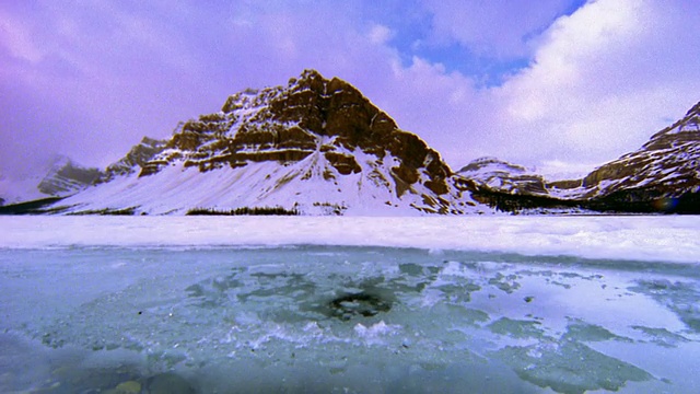 湖面上部分覆盖着冰+雪/雪山+背景中的时间流逝云+湖中的倒影视频素材