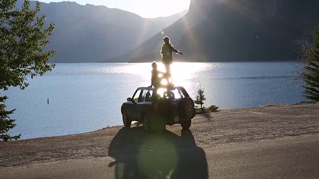 情侣站/坐在车顶上，眺望山下的湖泊视频素材