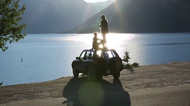 情侣站/坐在车顶上，眺望山下的湖泊视频下载