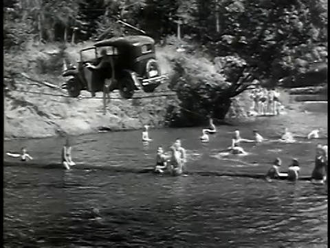 1932年B/W宽镜头汽车行驶在电缆上的河流与游泳者观看/人从汽车上跳下来视频下载