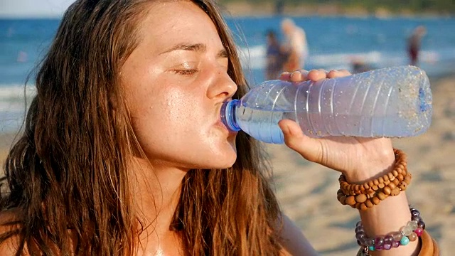 慢动作特写镜头，一个口渴的女孩在海滩上喝冷水视频下载