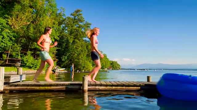 两名年轻女子在湖边甲板上乘坐橡皮艇享受夏天视频素材