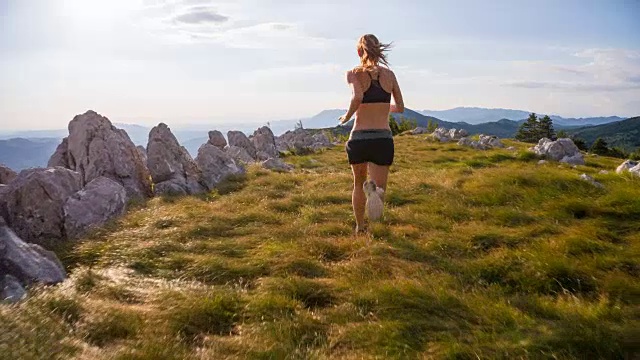 年轻的女运动员在山上的草地上跑步视频素材