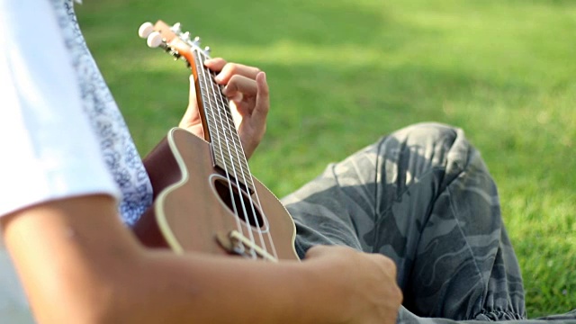 一个亚洲男孩在公园里弹奏四弦琴视频下载