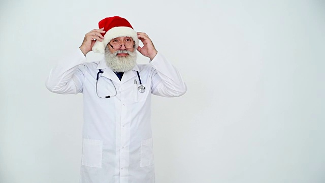 戴着圣诞老人帽的成年资深医生显示拷贝空间，灰色背景上竖起大拇指视频下载
