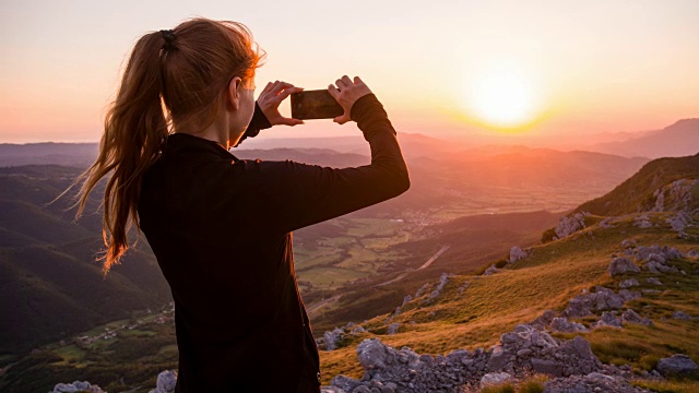 年轻女子用智能手机拍摄日落视频素材